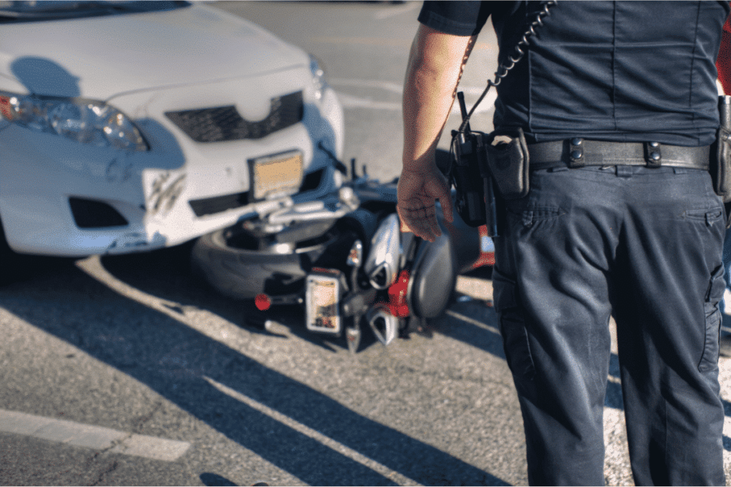 A police man looking at an accident scene involving a car and a motorcycle